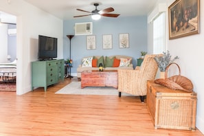 A living room with a sofa, a coffee table, a television, a ceiling fan, and a painting on the wall. - Pangola Cottage (Land O' Lakes)