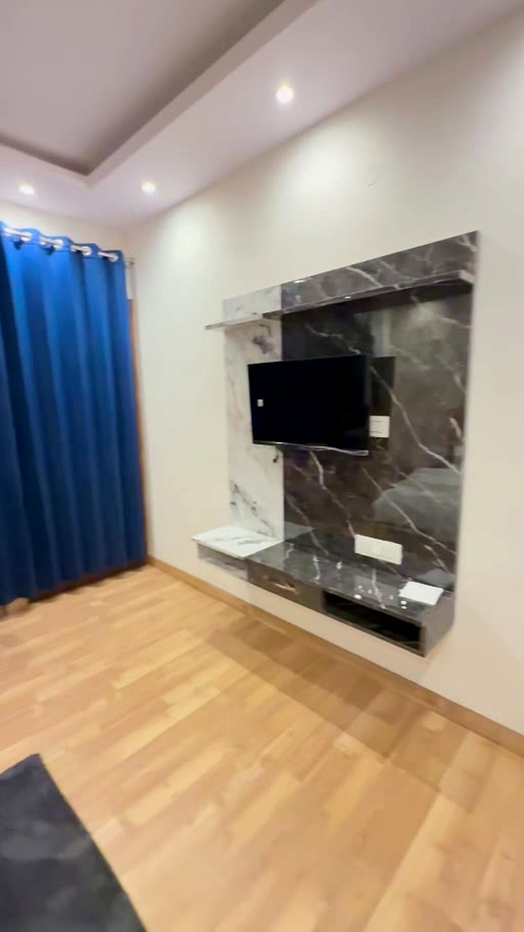 Un salon moderne avec un téléviseur à écran plat fixé à un mur de marbre, un plancher en bois et un rideau bleu.
