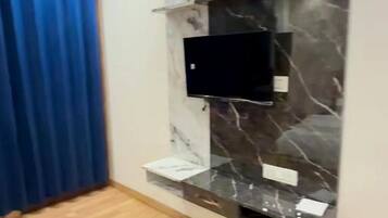 Un salon moderne avec un téléviseur à écran plat fixé à un mur de marbre, un plancher en bois et un rideau bleu.