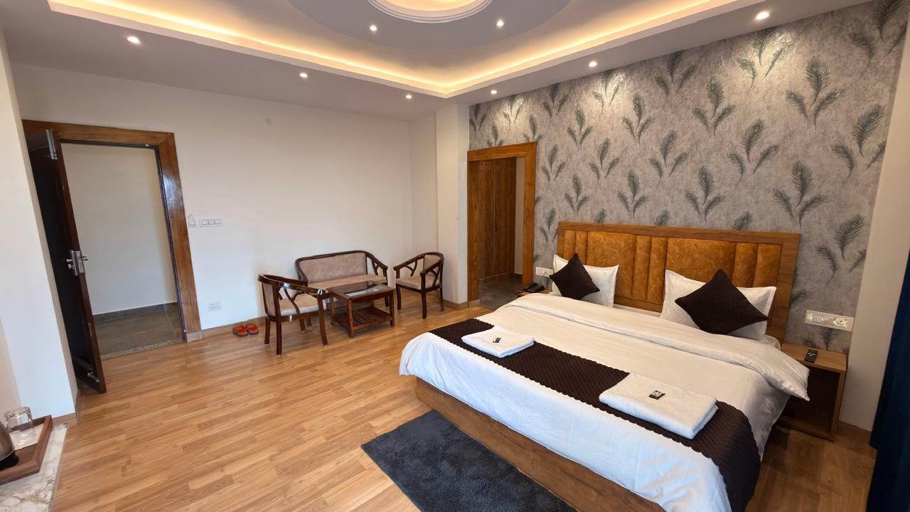 Une chambre d’hôtel avec un grand lit, une tête de lit en bois, un coin salon avec des fauteuils et un mur décoré de motifs.