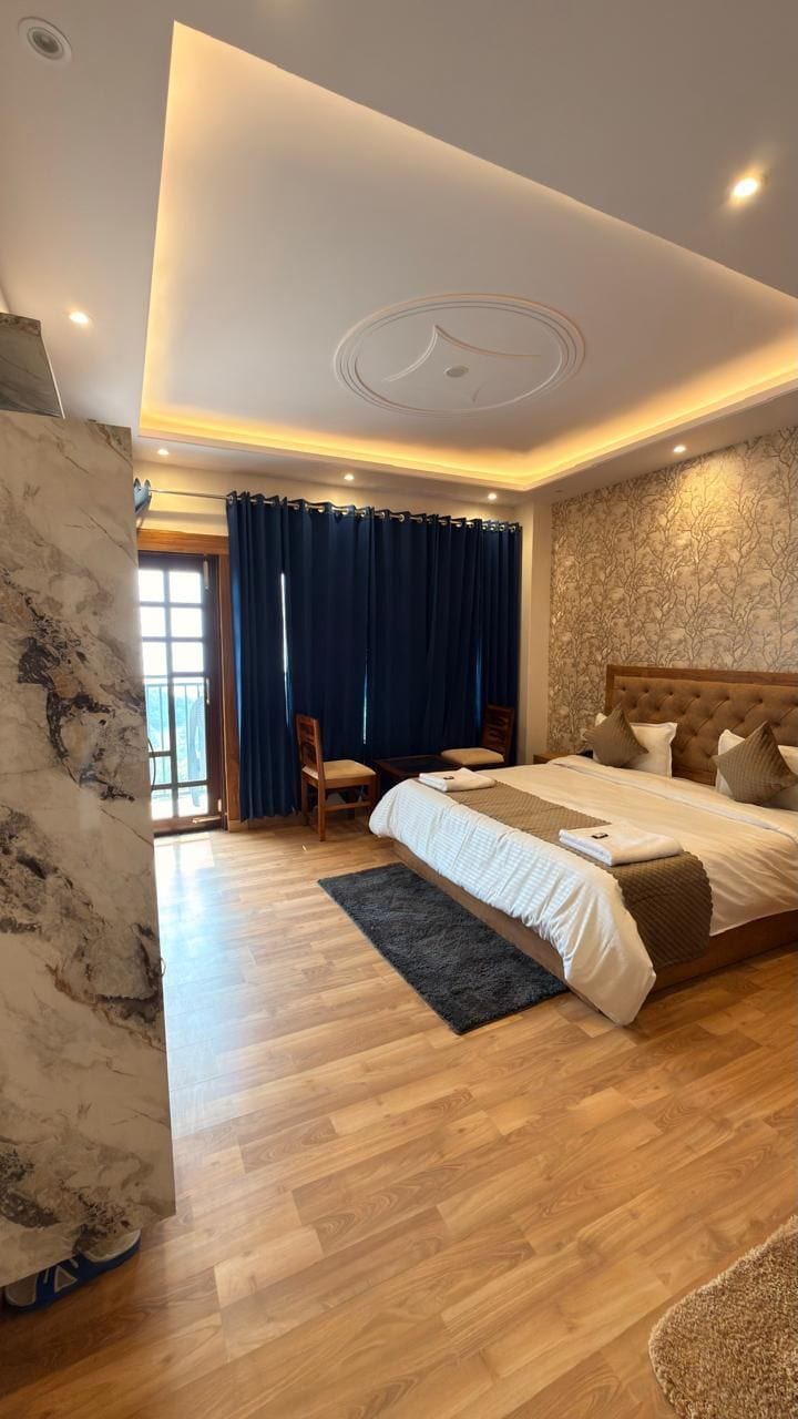 Un dormitorio moderno con una cama grande, piso de madera, techo con iluminación empotrada y vista al exterior a través de una ventana.