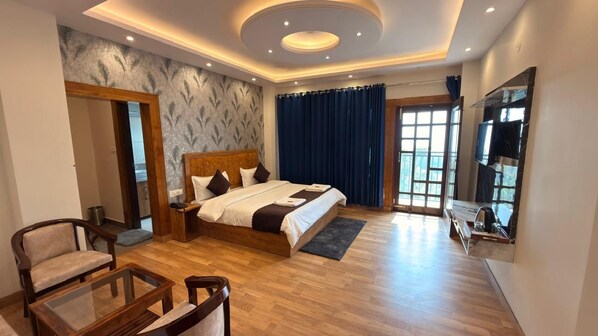 A modern bedroom with a large bed, a wooden chair, a glass table, and a TV mounted on the wall.