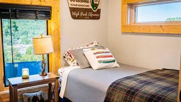 A bedroom with a bed, a nightstand, a lamp, a welcome sign, and a window with a view.