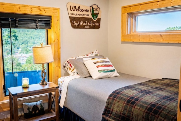 A bedroom with a bed, a nightstand, a lamp, a welcome sign, and a window with a view.