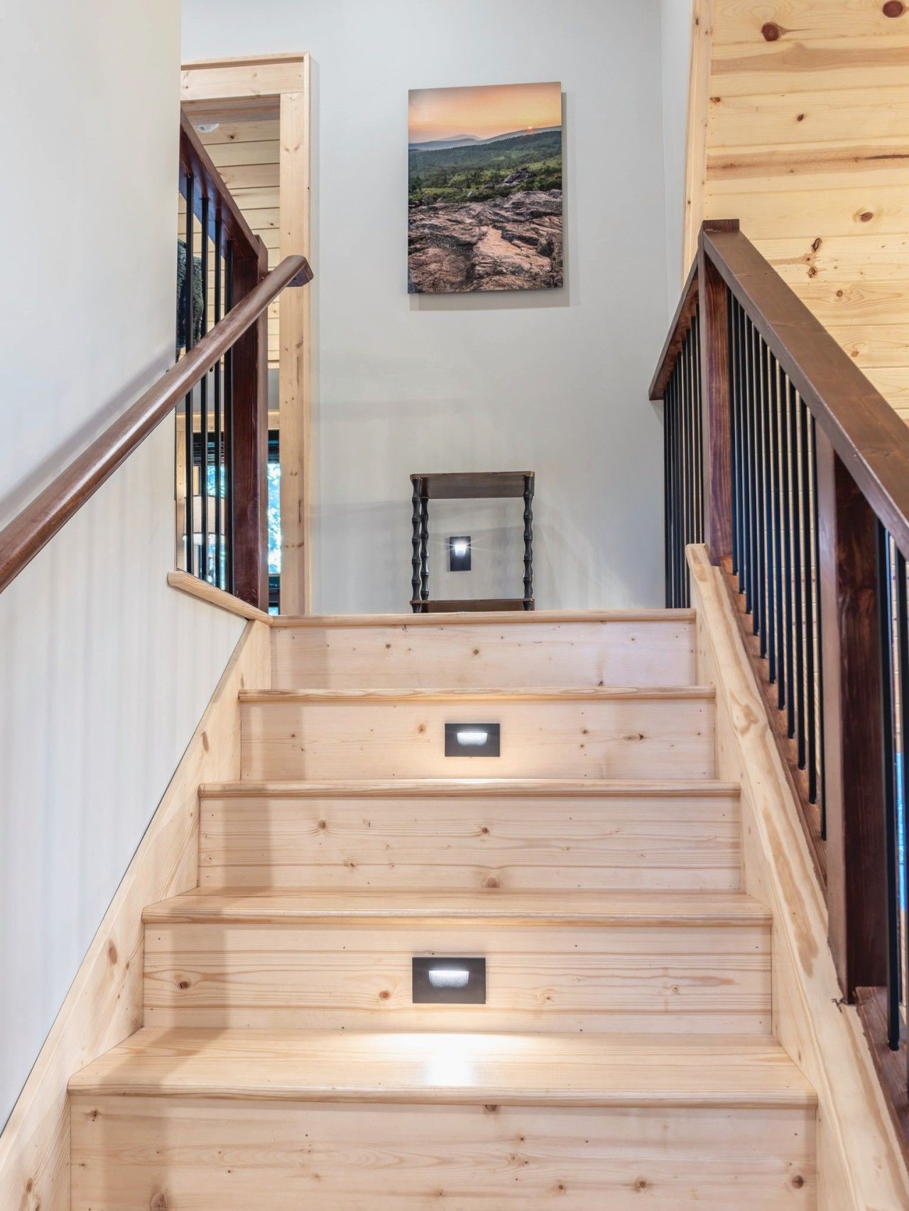 Un escalier en bois avec une rampe, un tableau accroché au mur et une petite table en bas.