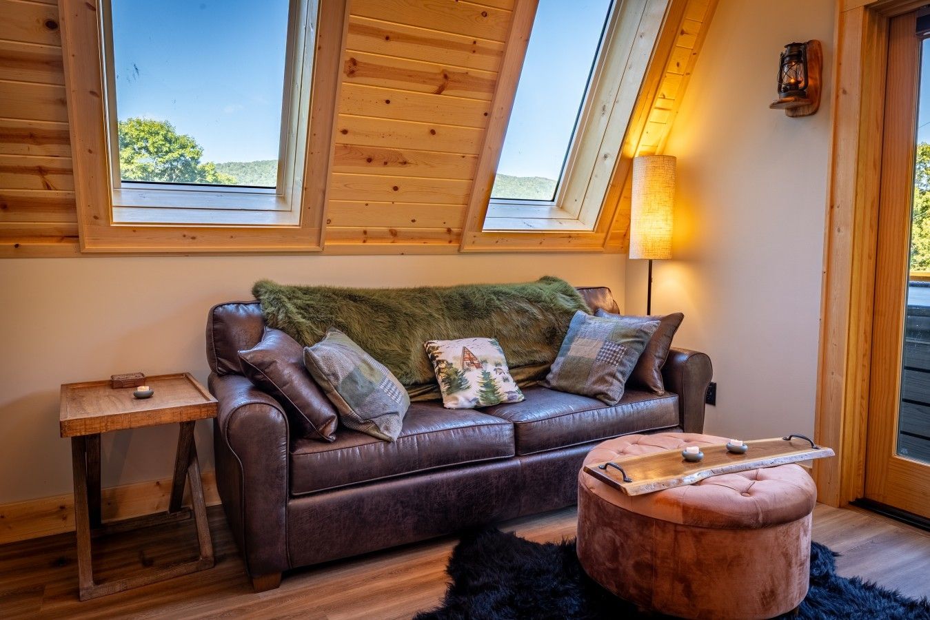 A cozy room with a leather sofa, a small side table, a round ottoman, and a lamp.