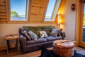 A cozy room with a leather sofa, a small side table, a round ottoman, and a lamp.