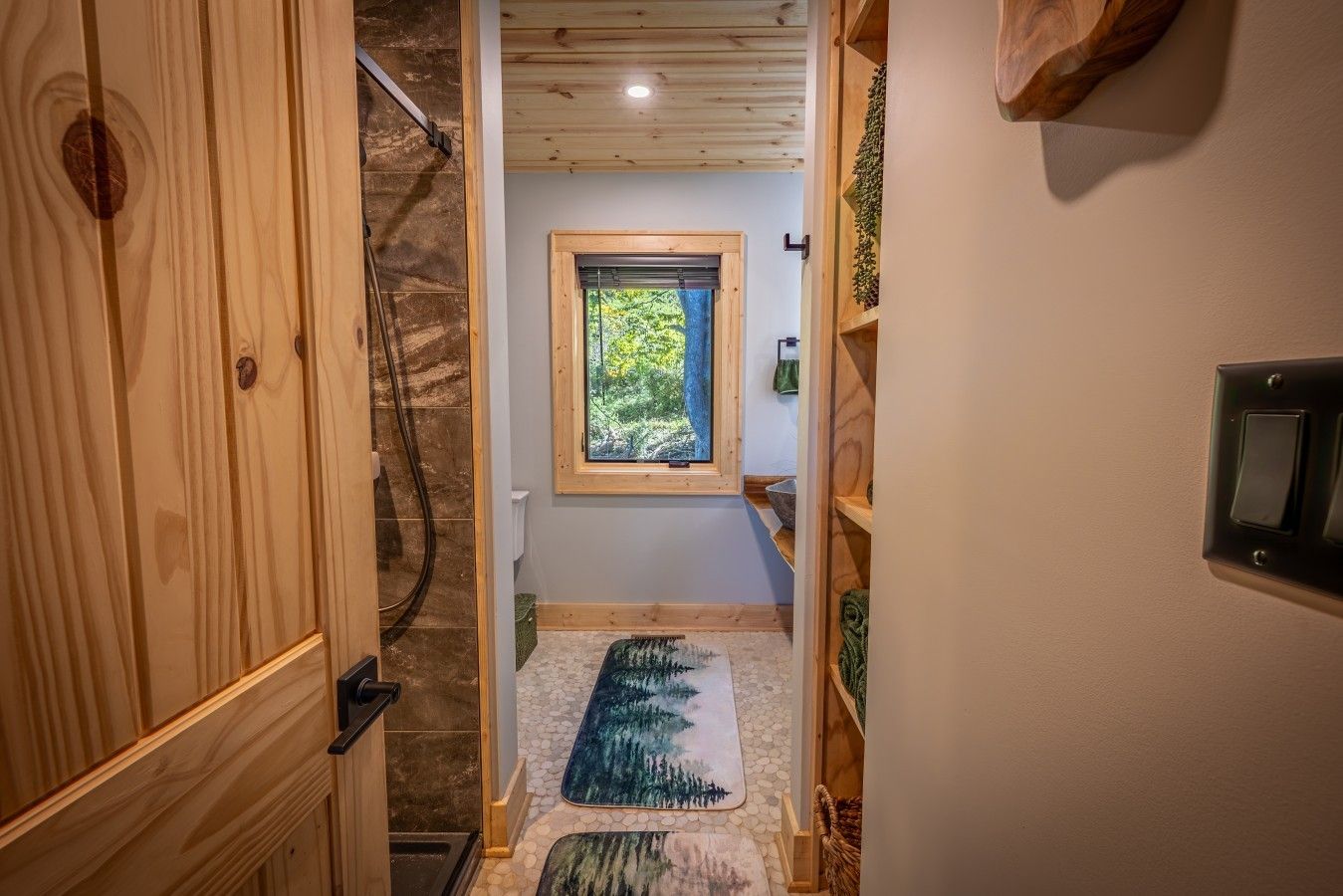 A wooden interior hallway leading to a bathroom with a window, a towel rack, and a switchboard.