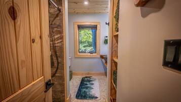 A wooden interior hallway leading to a bathroom with a window, a towel rack, and a switchboard.
