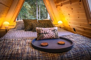 Una camera accogliente con un letto, cuscini, un vassoio con dei bottoni e una finestra vista foresta.