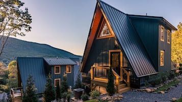 Eine moderne Hütte mit geneigtem Dach, einer Holzterrasse und einem Kiesweg.