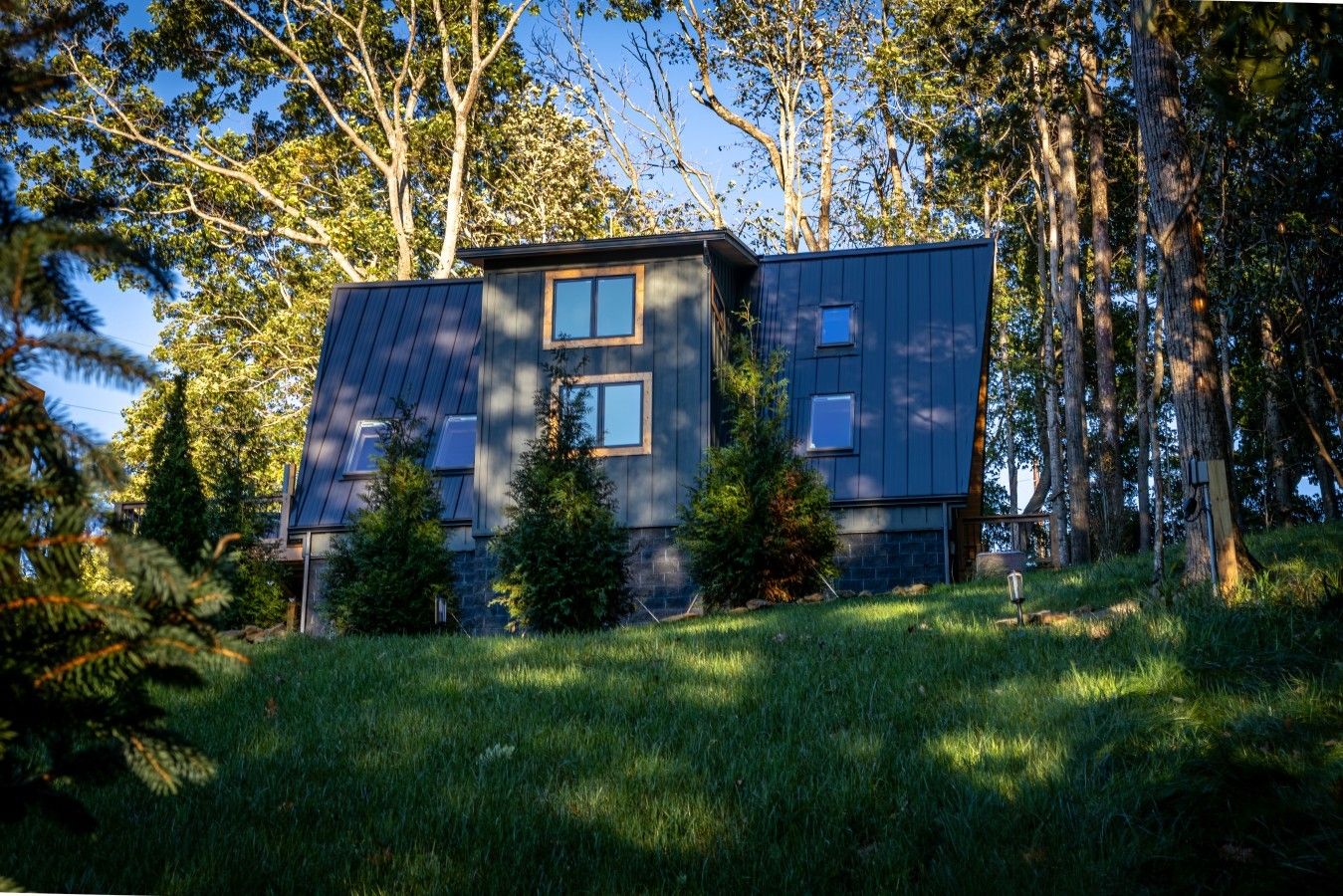 Une maison moderne avec un toit en pente, entourée d’arbres et d’une pelouse.