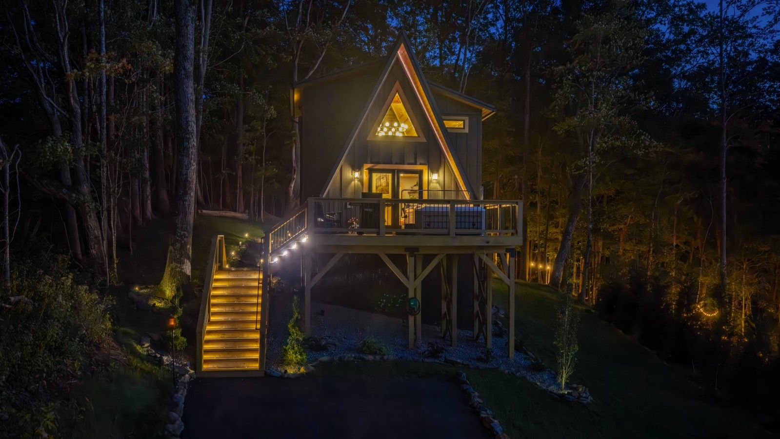 A cabin with a deck, surrounded by trees, and a staircase leading to the entrance.