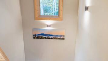 Un escalier en bois avec une rampe, une fenêtre donnant sur les arbres et un tableau encadré accroché au mur.