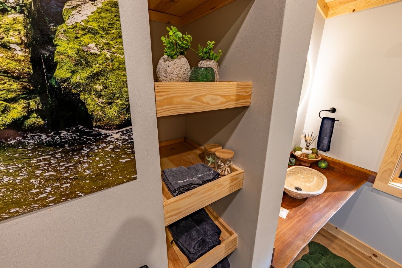 Une salle de bain avec une étagère en bois où sont rangées les serviettes, un lavabo avec un receveur en pierre et un porte-serviettes fixé au mur.