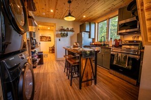 Una cucina con pavimento in legno, un'isola centrale con sgabelli, forno a incasso e un'ampia finestra.
