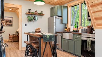 Eine moderne Küche mit Holzbalkendecke, einer Essecke mit Hockern und einem Kühlschrank.