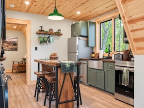 A modern kitchen with a wooden ceiling, a dining area with stools, and a refrigerator.