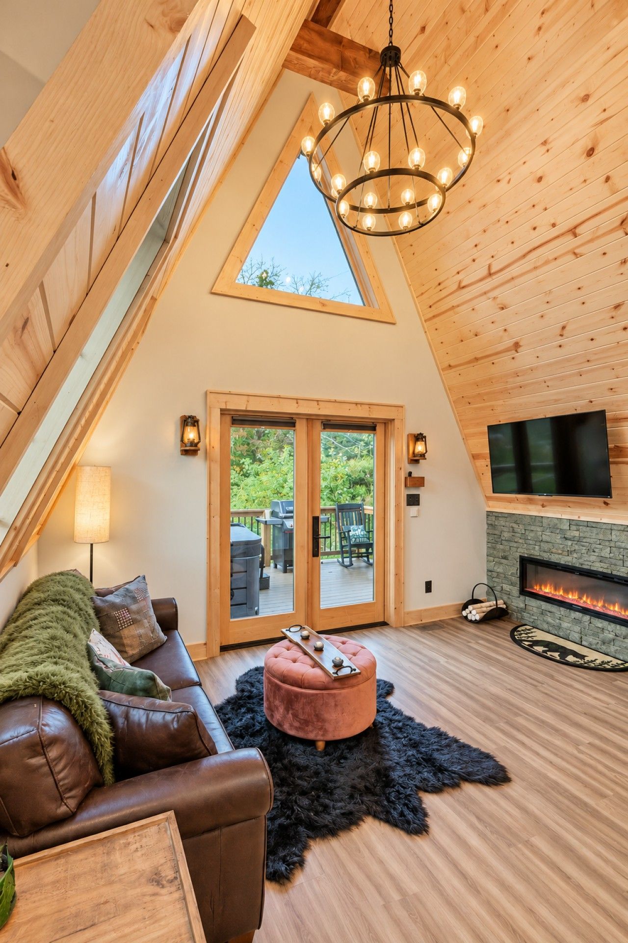 A cozy loft-style room with a sloped ceiling, a fireplace, a television, and a large window overlooking a deck.