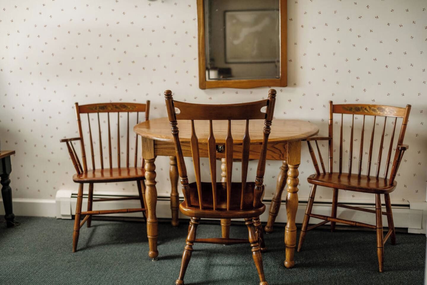 Une table à manger avec quatre chaises en bois, un miroir au mur et un papier peint à motifs.