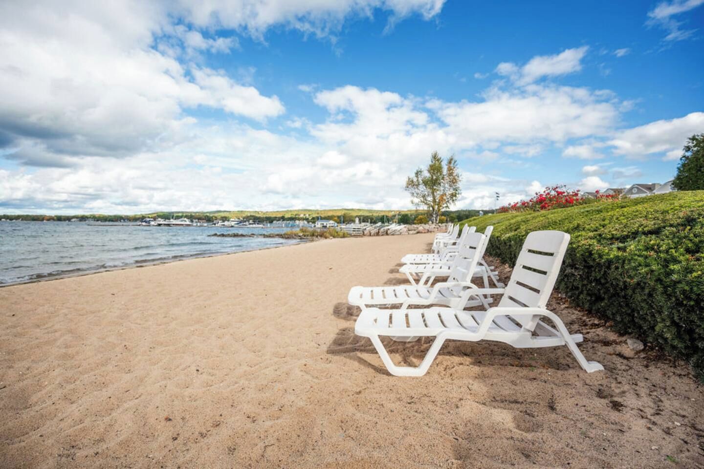Une plage avec des chaises longues blanches et une vue sur l’eau et les bateaux au loin.