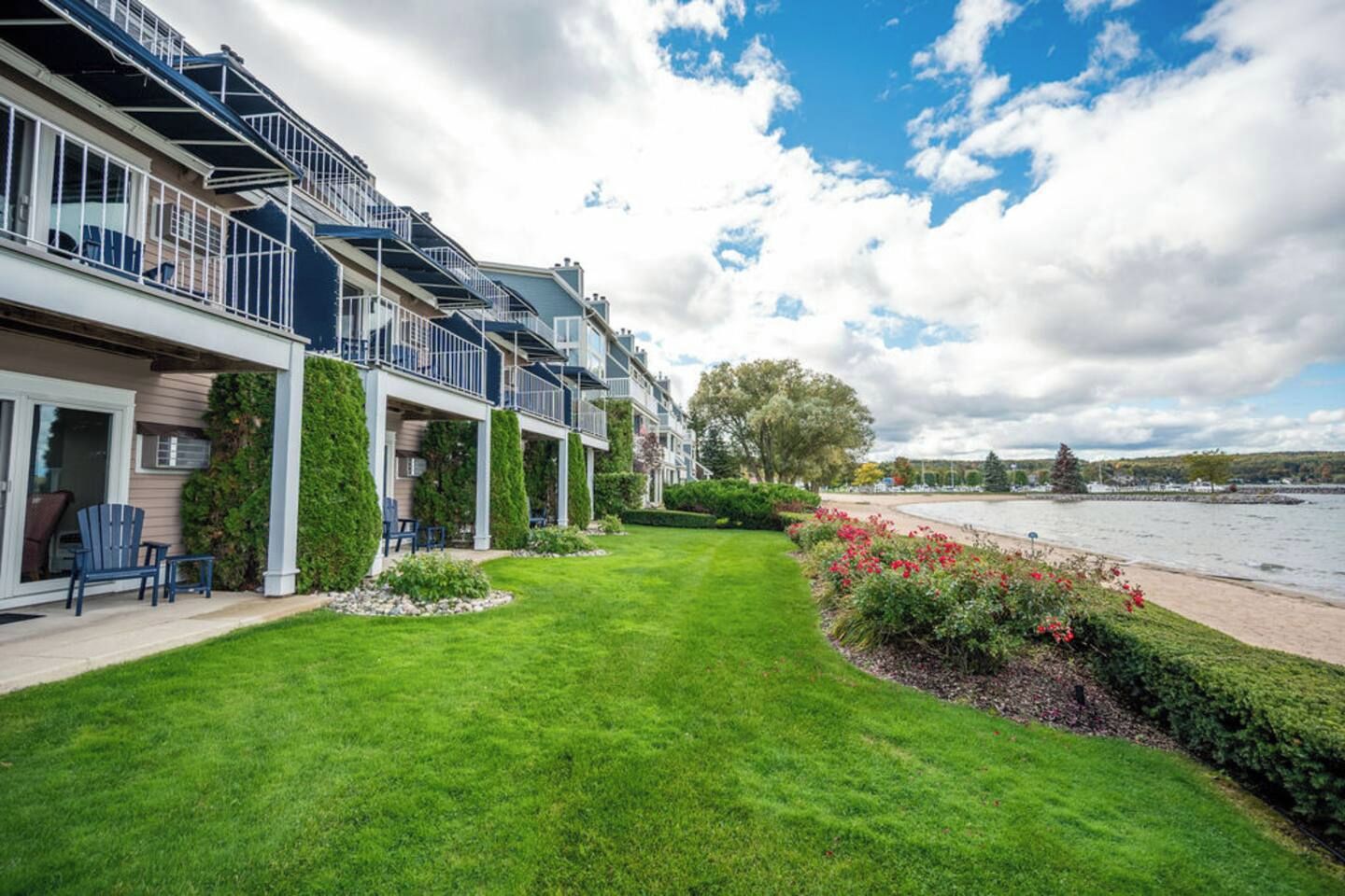 Une rangée d’immeubles modernes à plusieurs étages, dotés de balcons, avec une pelouse bien entretenue et une vue sur la rivière.