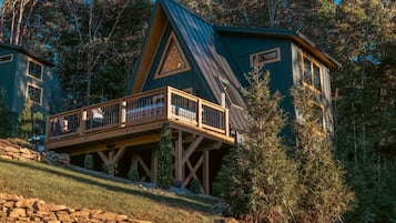Eine Holzhütte mit einer Holzterrasse und einem steilen Satteldach, umgeben von Bäumen.