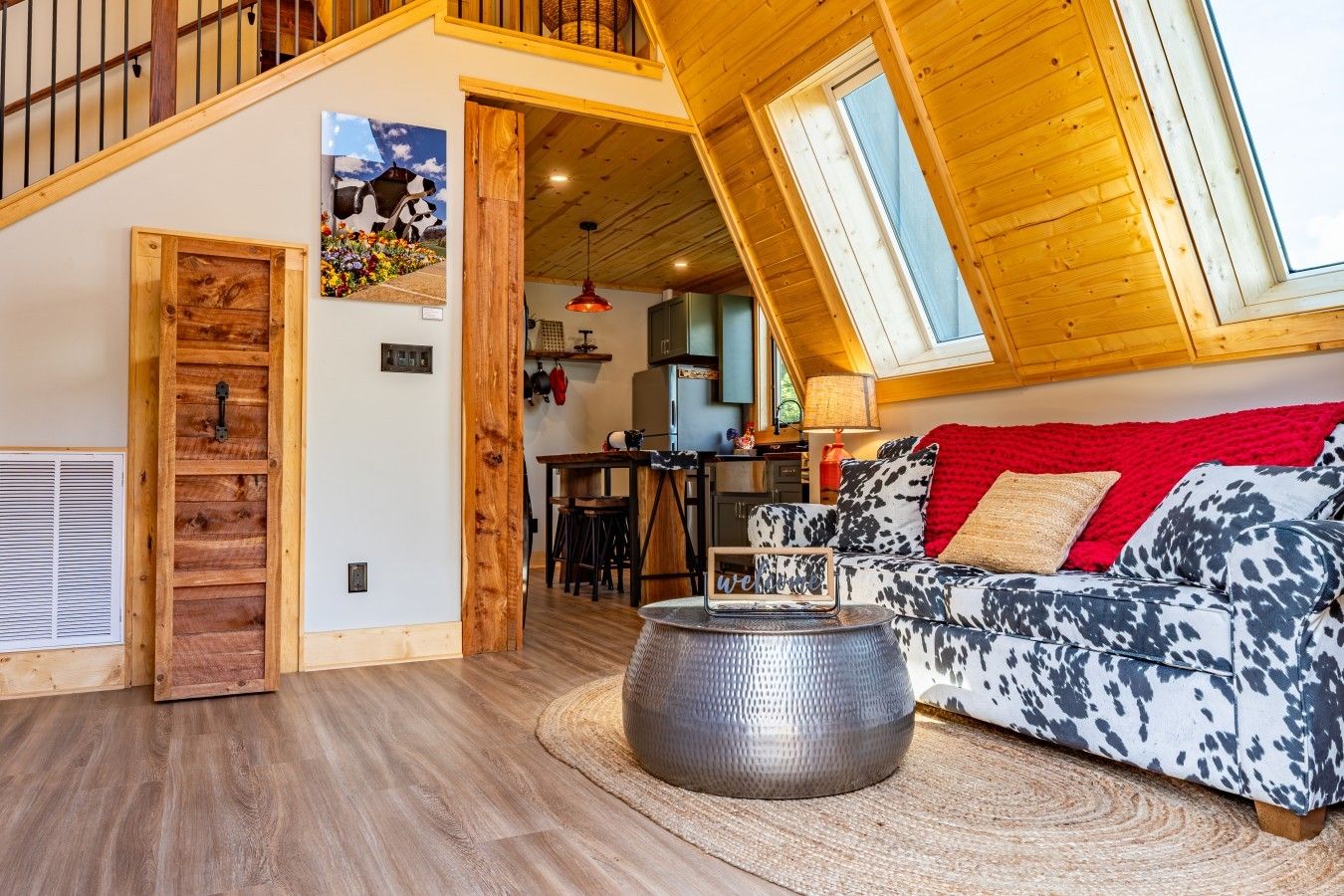 Un salon chaleureux avec un plafond en pente, une porte en bois, un coin repas et une cuisine à l’arrière-plan.