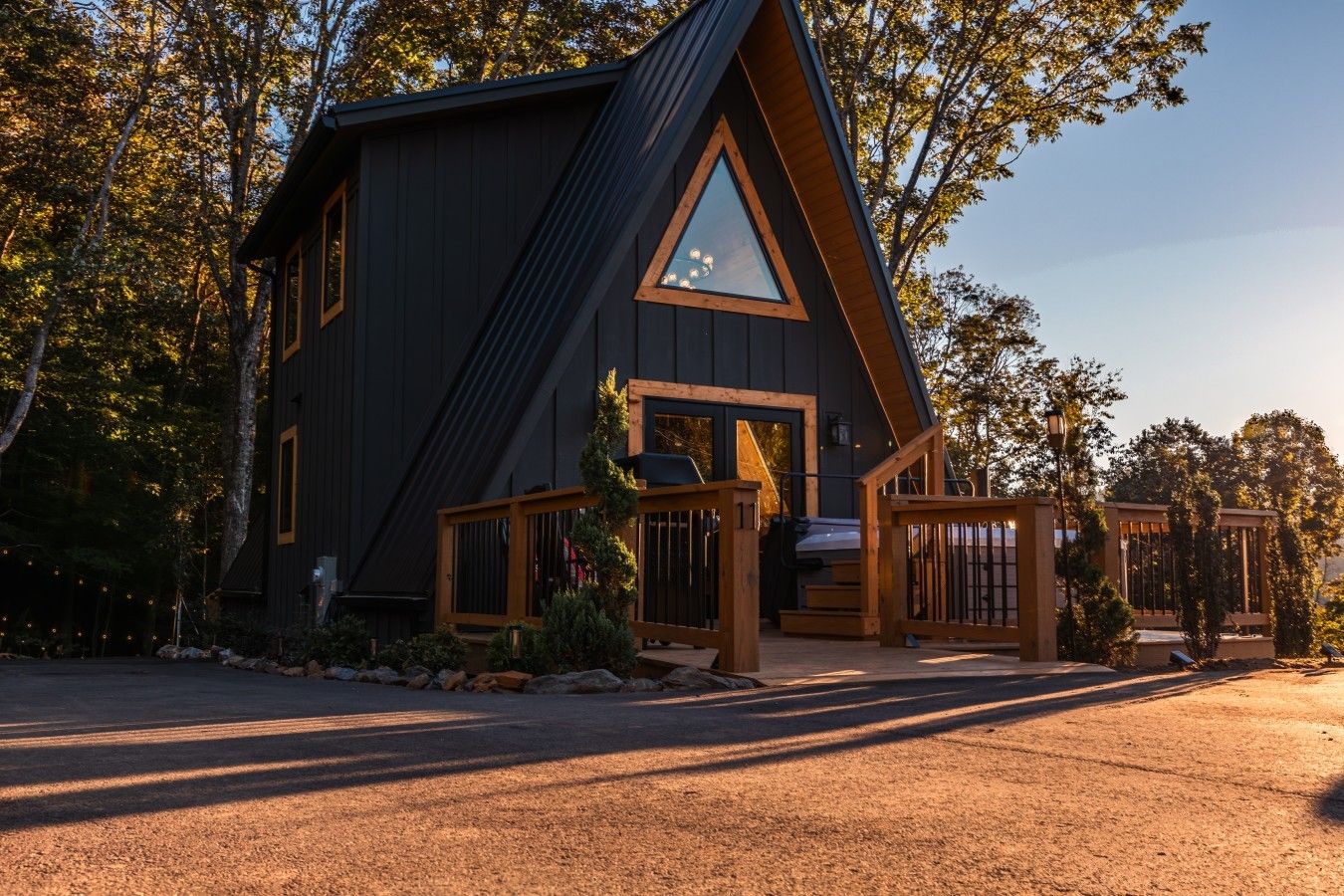 A modern, dark-colored cabin with a triangular roof, a wooden deck, and a large window.