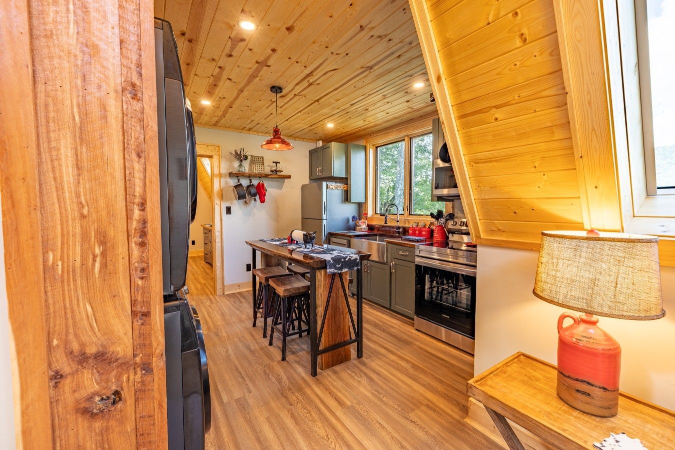 A modern kitchen with wooden floors, a dining area with stools, and a large window providing natural light.
