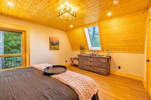 Una camera da letto con un letto grande, una cassettiera, una finestra vista alberi e una lampada a sospensione al soffitto.