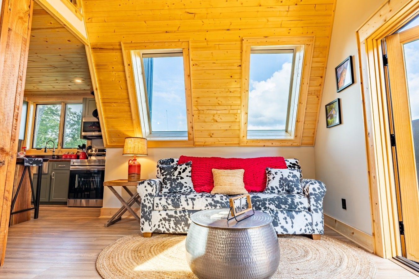 Un accogliente interno di una baita con soffitto in legno, un divano con una coperta rossa, un'area pranzo con tavolo e sedie, e una cucina con elettrodomestici moderni.