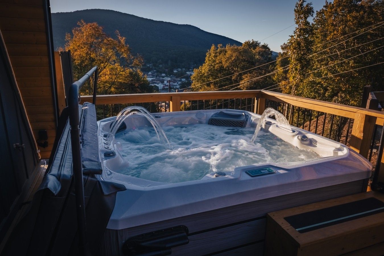 A hot tub on a wooden deck with a view of a mountain and trees.