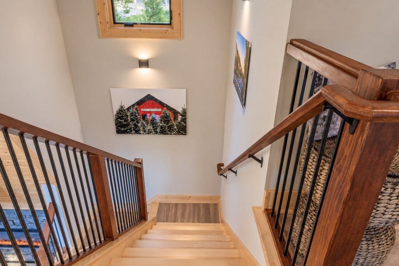 A wooden staircase with a handrail, a wall-mounted picture, and a small window at the top.