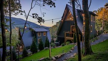 A cabin with a sloped roof, a deck, and a view of the surrounding forest and mountains.