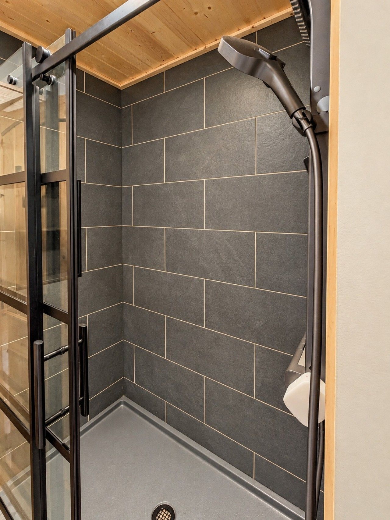 A modern bathroom with dark tiled walls, a glass shower enclosure, and a visible showerhead.