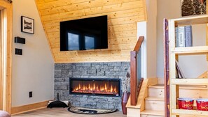 Um quarto com lareira, televisão na parede e estante de livros.