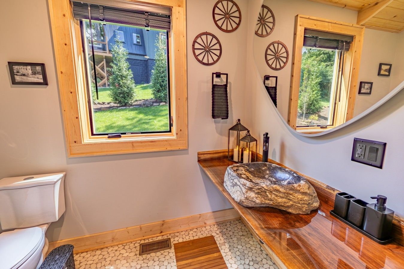 A bathroom with a stone basin, wooden floor, and a window with a view of a house and trees.
