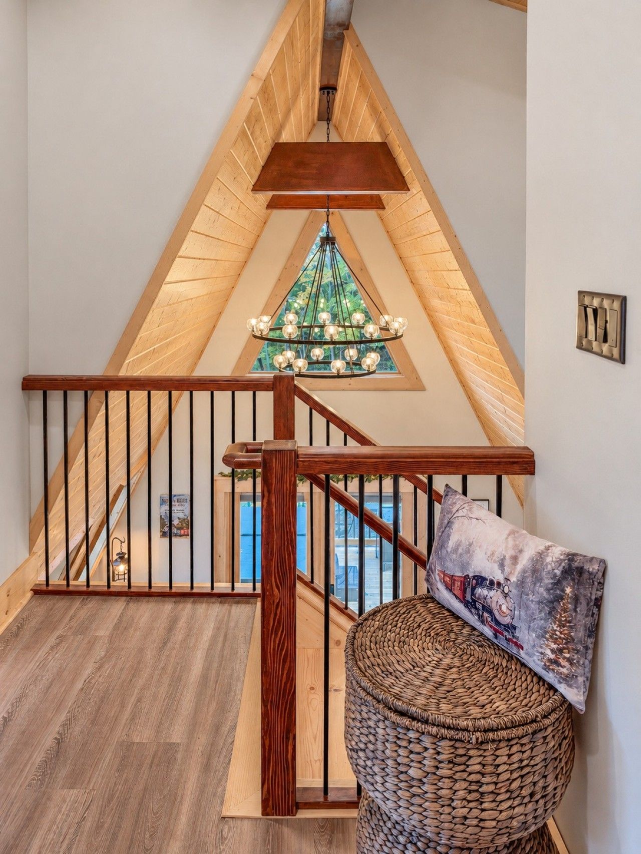 A wooden staircase with a railing, a hanging light fixture, and a wicker basket with a cushion.