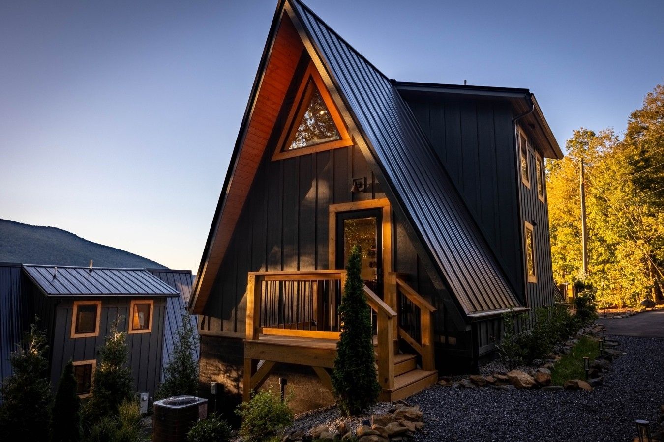 A modern cabin with a steeply pitched roof, a wooden deck, and a stone pathway leading to the entrance.