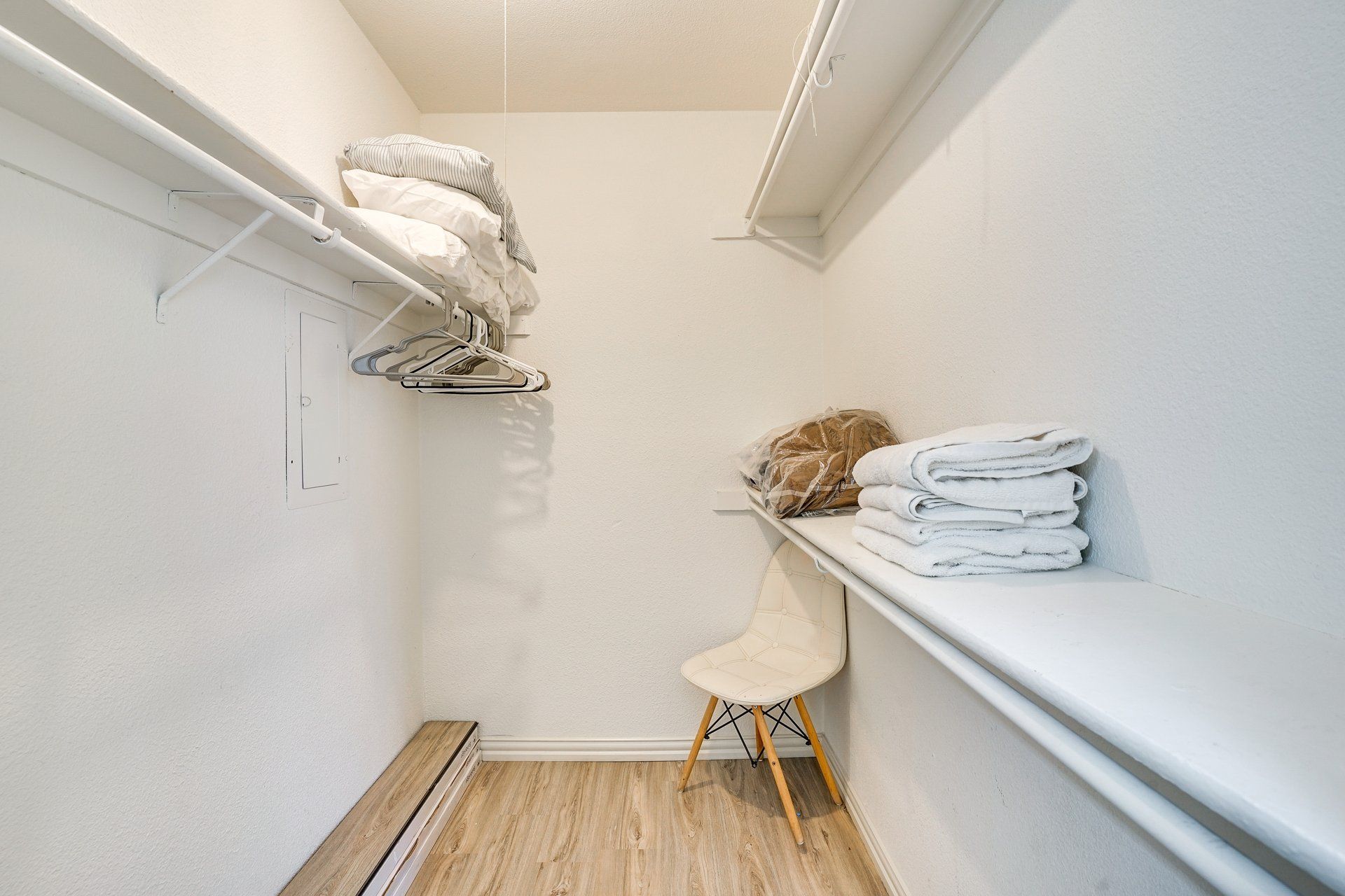 A narrow walk-in closet with a wooden floor, a white chair, and a shelf with folded towels.