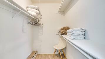 A narrow walk-in closet with a wooden floor, a white chair, and a shelf with folded towels.