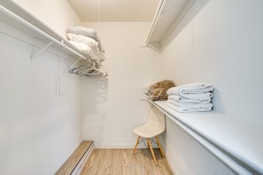 Een smalle inloopkast met een houten vloer, een witte stoel en een plank met opgevouwen handdoeken.