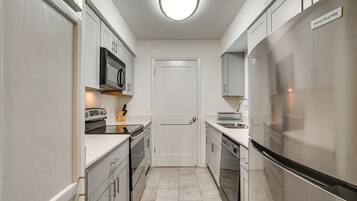 A narrow kitchen with white cabinets, a built-in oven, a microwave, and a stainless steel refrigerator.
