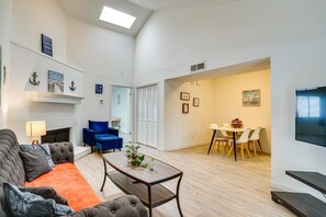 Een woonkamer met een bank, fauteuil en salontafel, een eethoek met een tafel en stoelen, en een aan de muur bevestigde televisie.