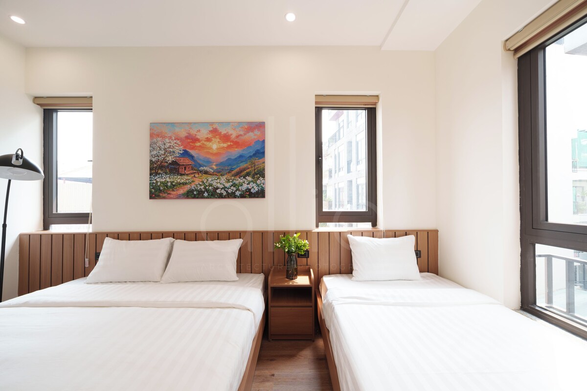 Habitación de hotel con dos camas, un cuadro en la pared y una ventana con vista a edificios.