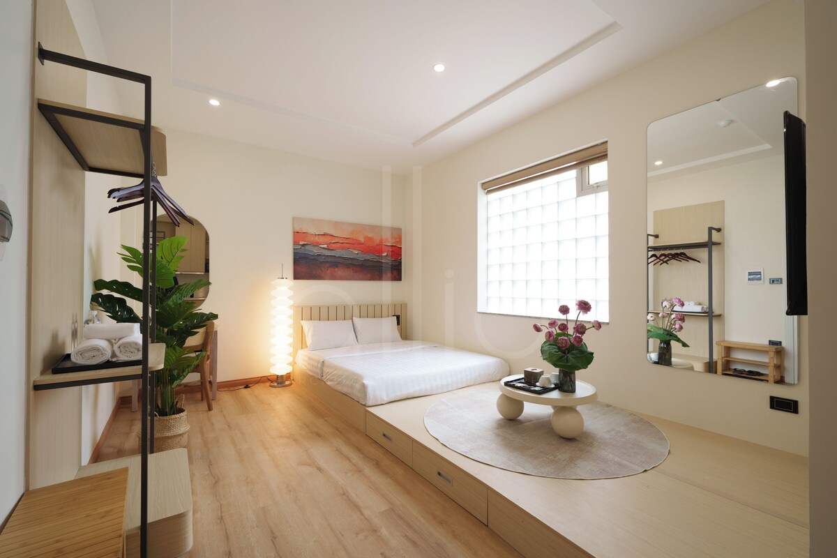 Una habitación de hotel moderna con una cama, una mesita de noche y un ventanal grande.