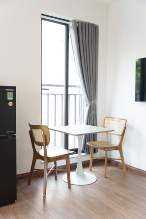 Una habitación con una mesa, dos sillas, un televisor montado en la pared y una ventana con cortinas.