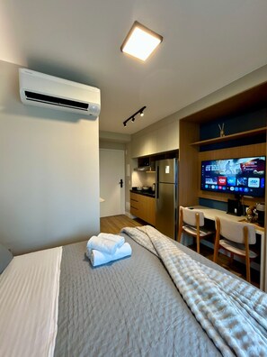 A hotel room with a bed, a TV, a kitchenette, and an air conditioning unit. - Level Brooklin 1217 (São Paulo)