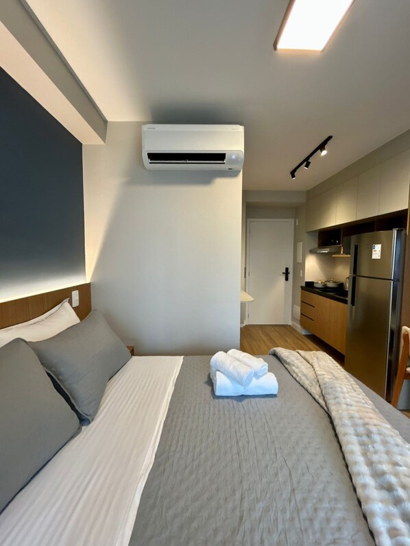 Ein Hotelzimmer mit einem Bett, einem Flachbildfernseher, einer Klimaanlage, einer Küchenzeile mit einem Kühlschrank und einem Holzkopfende.